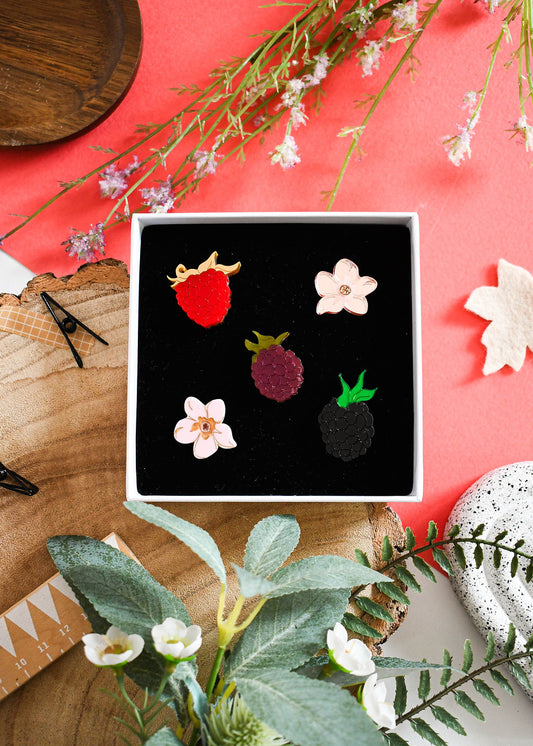 Set of earrings with floral and berry designs in a box on a decorative background with flowers and wood.