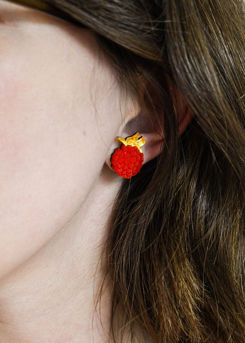 Close-up of a person wearing a red bramble berry earring with gold accents.