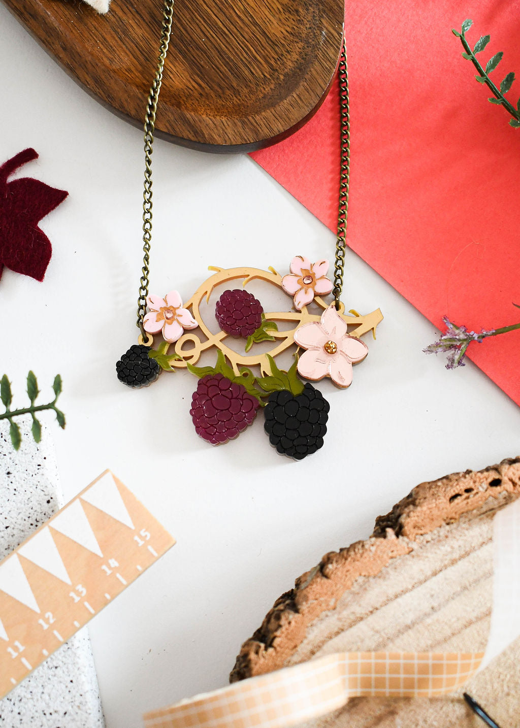 Necklace with floral and berry design on a white surface with decorative elements